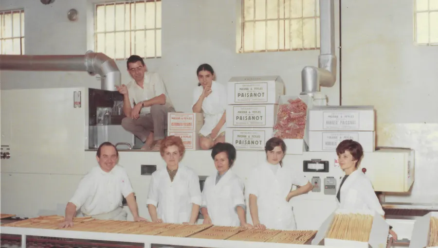 Archive colour photo: seven people from the bakery, nearly all in white coats, behind the bench with grissini laid out on it and boxes stacked behind them